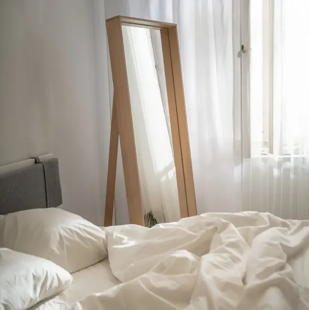 Lustro opierające się o ścianę w minimalistycznej sypialni.